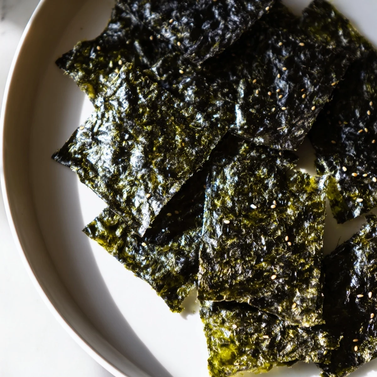 Golden-brown roasted seaweed chips arranged in a crisp, single layer on a white plate, showcasing their light, savory crunch and vibrant green hue.
