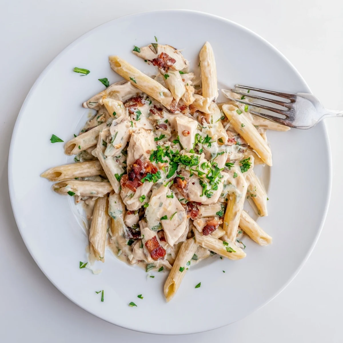A close-up of Creamy Chicken Bacon Penne, garnished with parsley and served alongside a glass of white wine.  