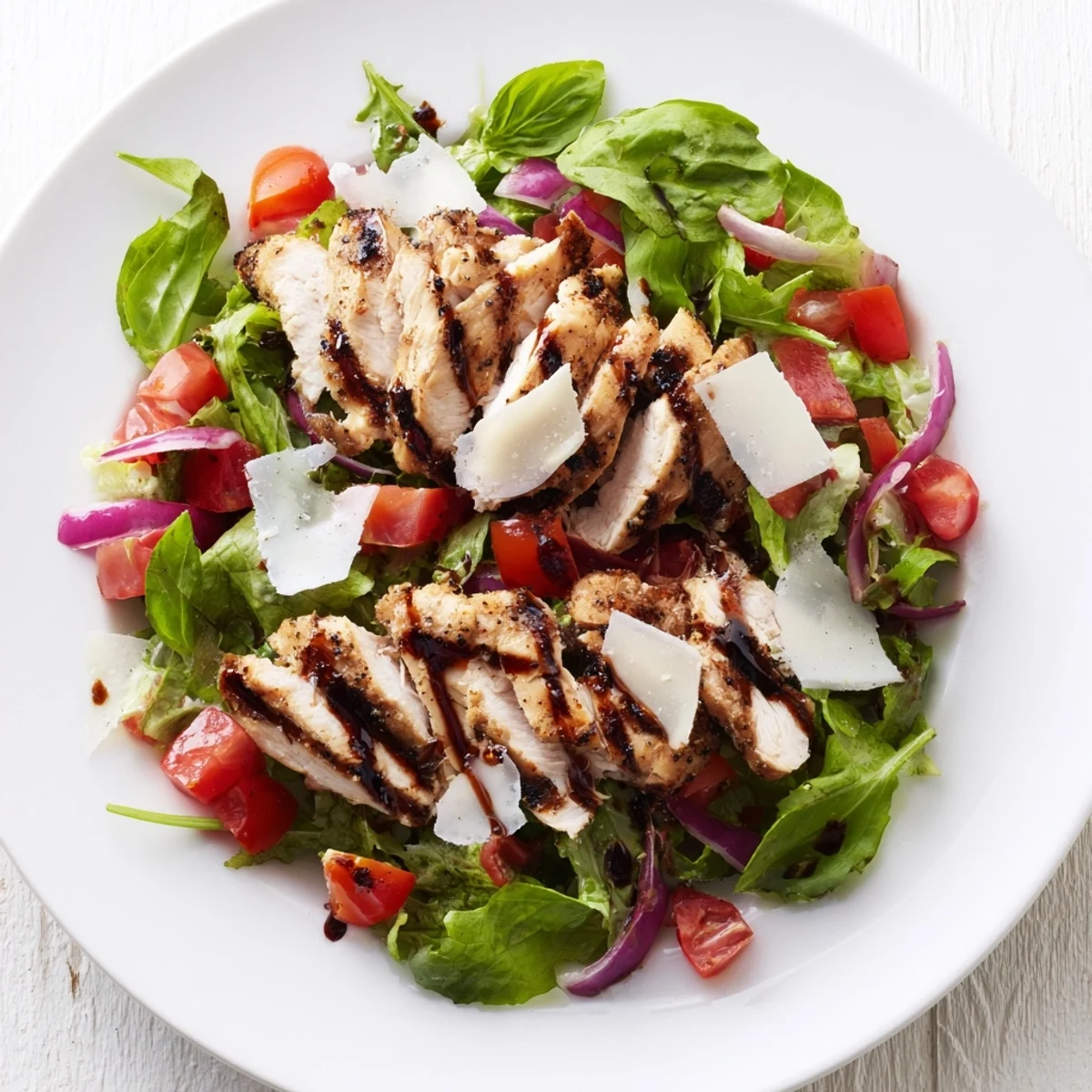 Grilled chicken slices topped with fresh tomato and basil bruschetta on a bed of mixed greens, served on a white plate.
