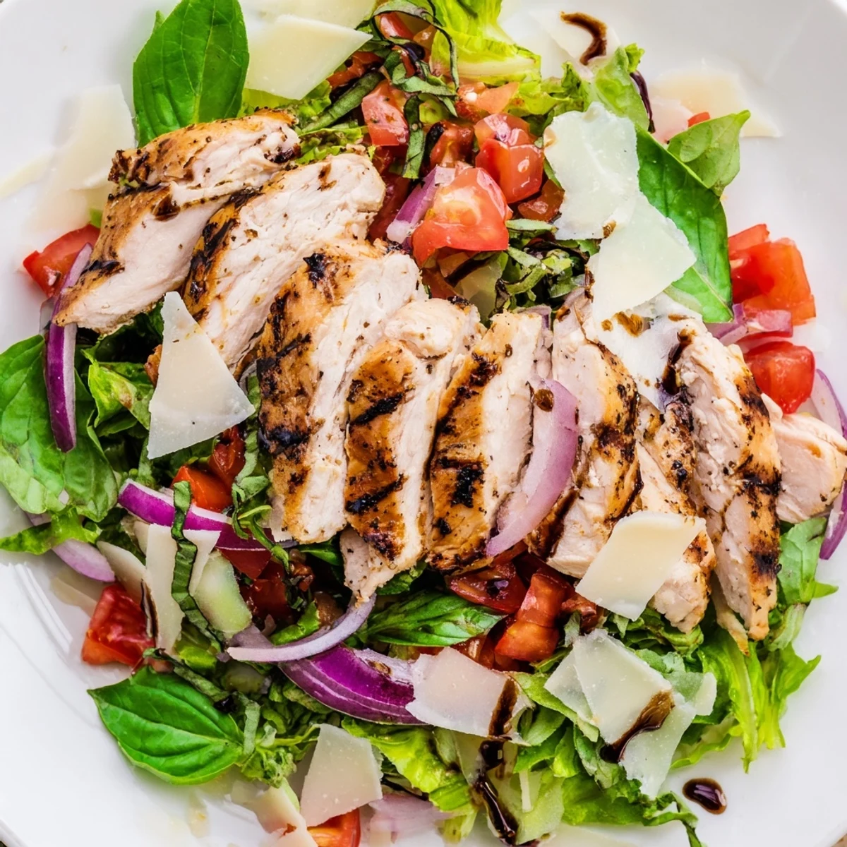 A close-up of sliced bruschetta chicken salad with zesty tomato topping, crisp greens, and a lemon wedge on the side.