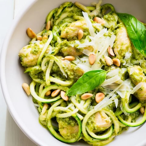 Golden-brown sautéed chicken tossed with fresh zucchini noodles and vibrant basil pesto in a serving bowl.  