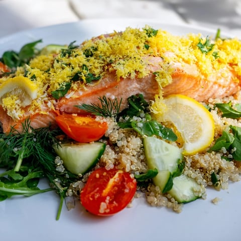 Flaky baked salmon fillet rests atop a vibrant quinoa salad with mixed greens and fresh herbs, drizzled with lemon vinaigrette.