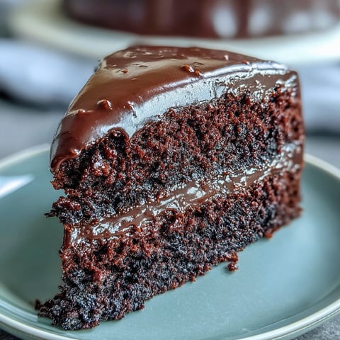 Freshly baked Easy Chocolate Fudge Cake layers with glossy, silky-smooth chocolate icing on a rustic plate.