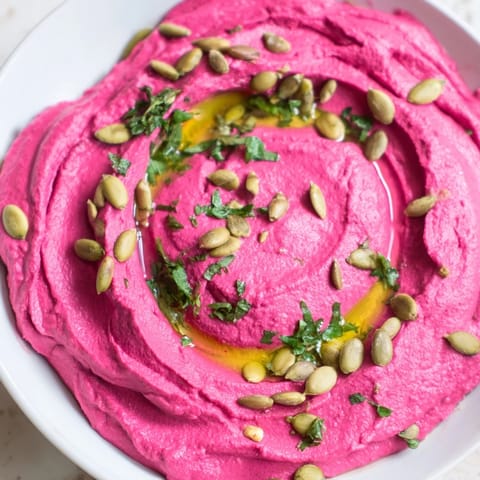 Roasted beet hummus swirl in a white bowl, paired with crisp cucumber slices and warm pita bread for a colorful, healthy snack.