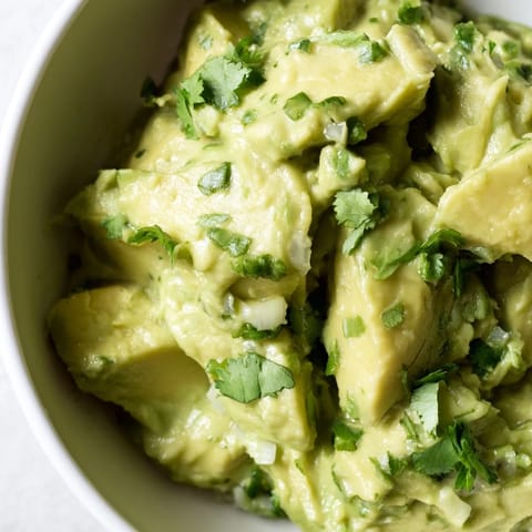 Fresh avocado lime dip in a white bowl, topped with cilantro and jalapeño, ready for dipping veggies or chips.