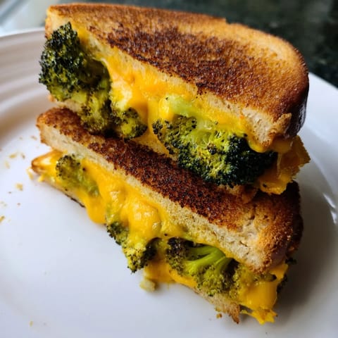 A close-up view shows the crispy, buttery exterior of the Roasted Broccoli & Cheddar Grilled Cheese, with gooey cheese pulling away from the bread.
