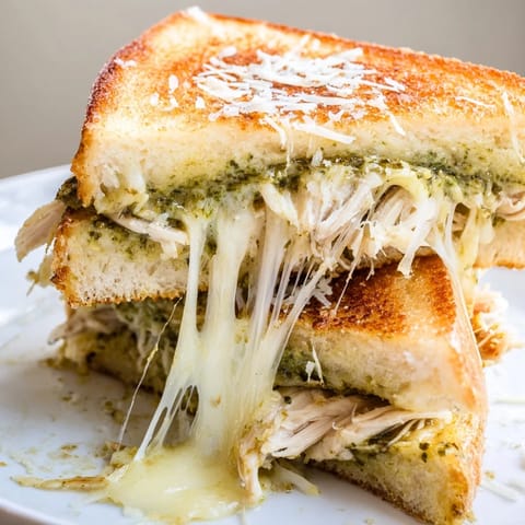 A close-up view of a Mozzarella Pesto Chicken Grilled Cheese, with gooey mozzarella stretching between slices of crusty bread.