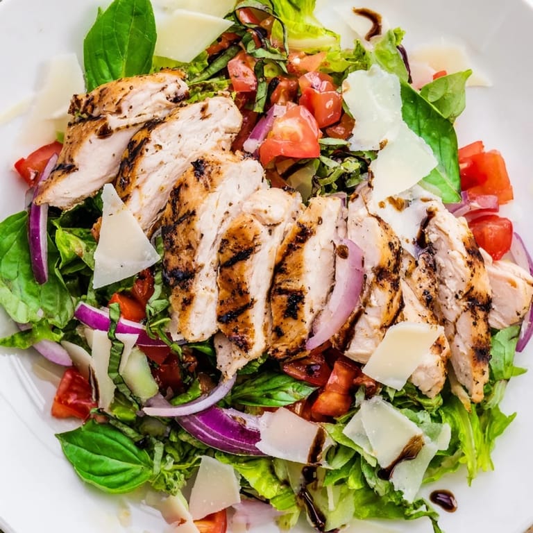 A close-up of sliced bruschetta chicken salad with zesty tomato topping, crisp greens, and a lemon wedge on the side.