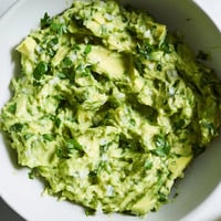 Creamy avocado lime dip garnished with cilantro and lime wedges, served with crunchy tortilla chips and fresh vegetable sticks.